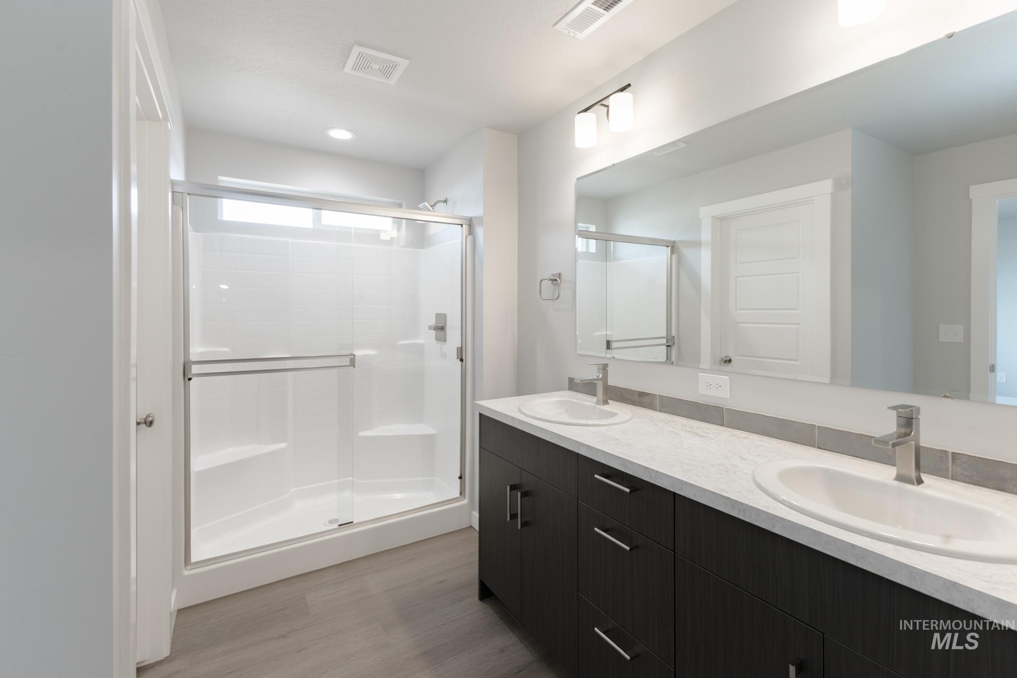 Bathroom with double vanity, light wood-style flooring, and a shower stall