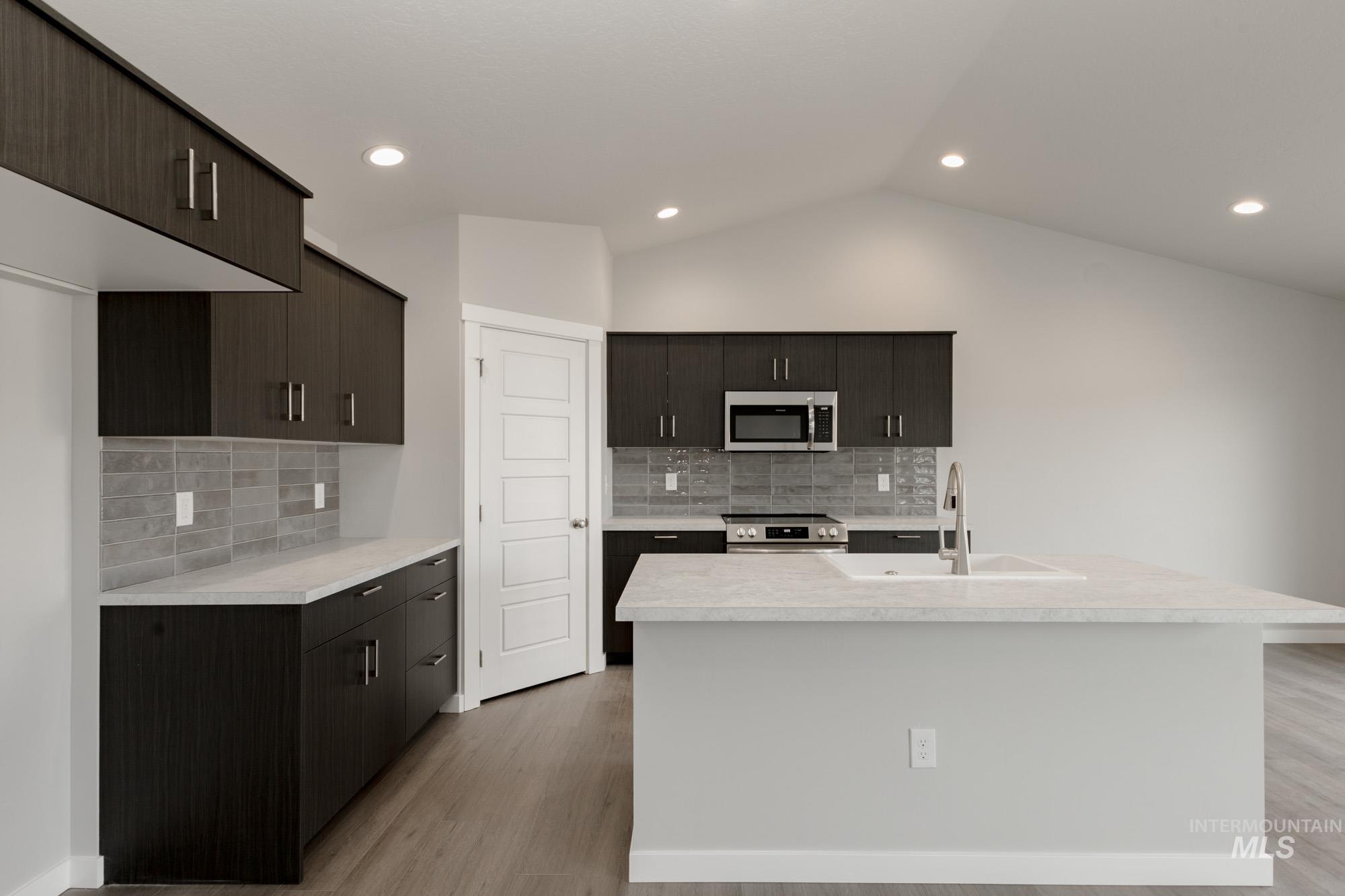 Kitchen with tasteful backsplash, stainless steel appliances, light wood-style floors, an island with sink, and recessed lighting