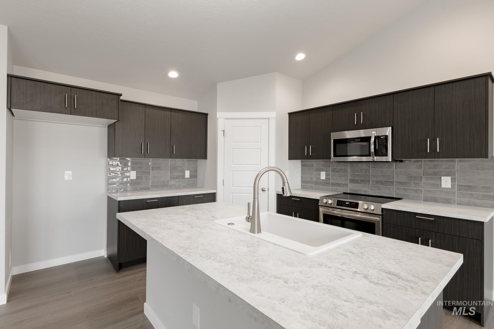 Kitchen featuring light countertops, stainless steel appliances, dark brown cabinetry, an island with sink, and recessed lighting