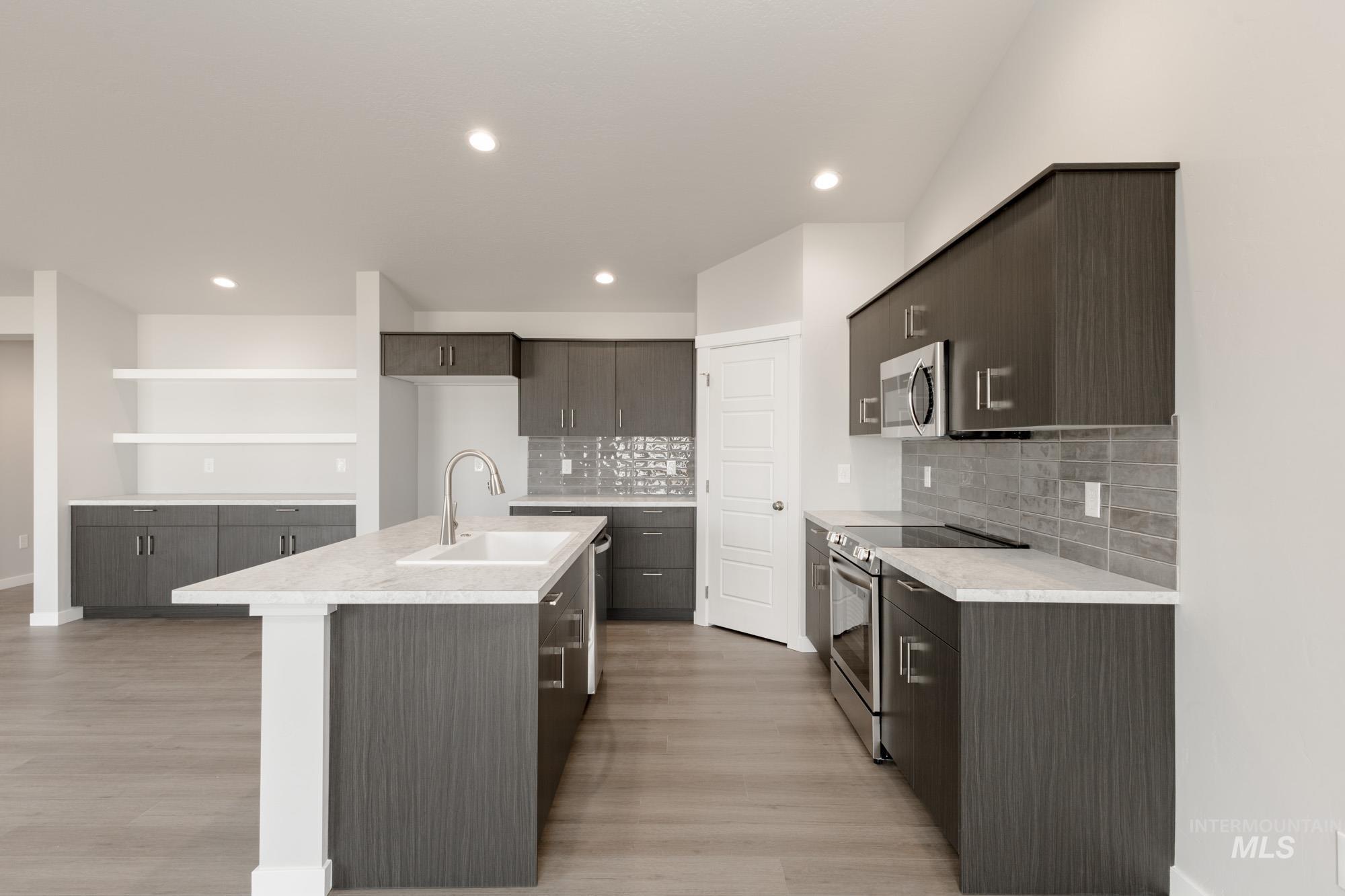 Kitchen with stainless steel appliances, a kitchen island with sink, tasteful backsplash, light wood-style flooring, and recessed lighting