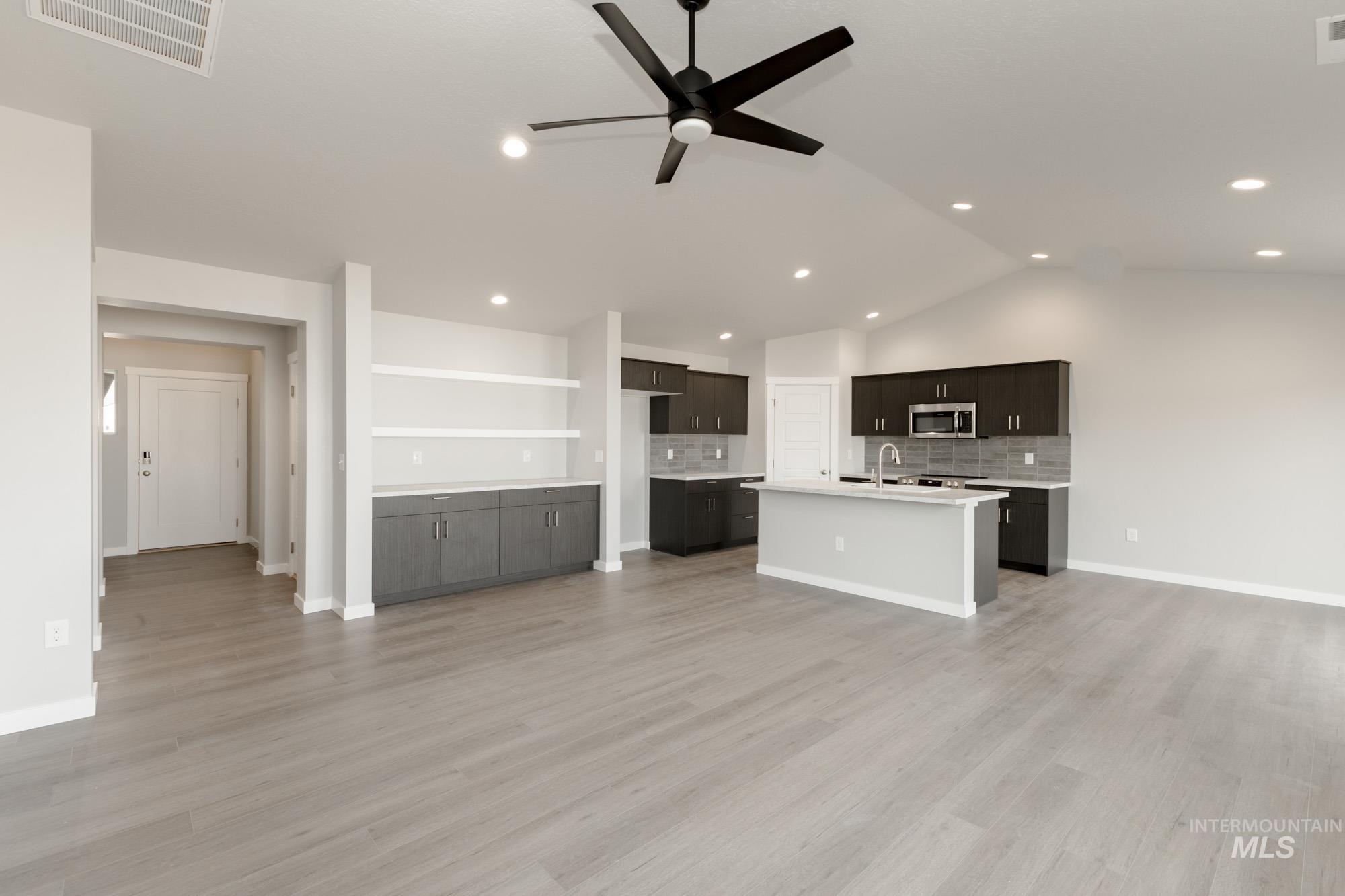 Kitchen with tasteful backsplash, open floor plan, vaulted ceiling, ceiling fan, and stainless steel microwave