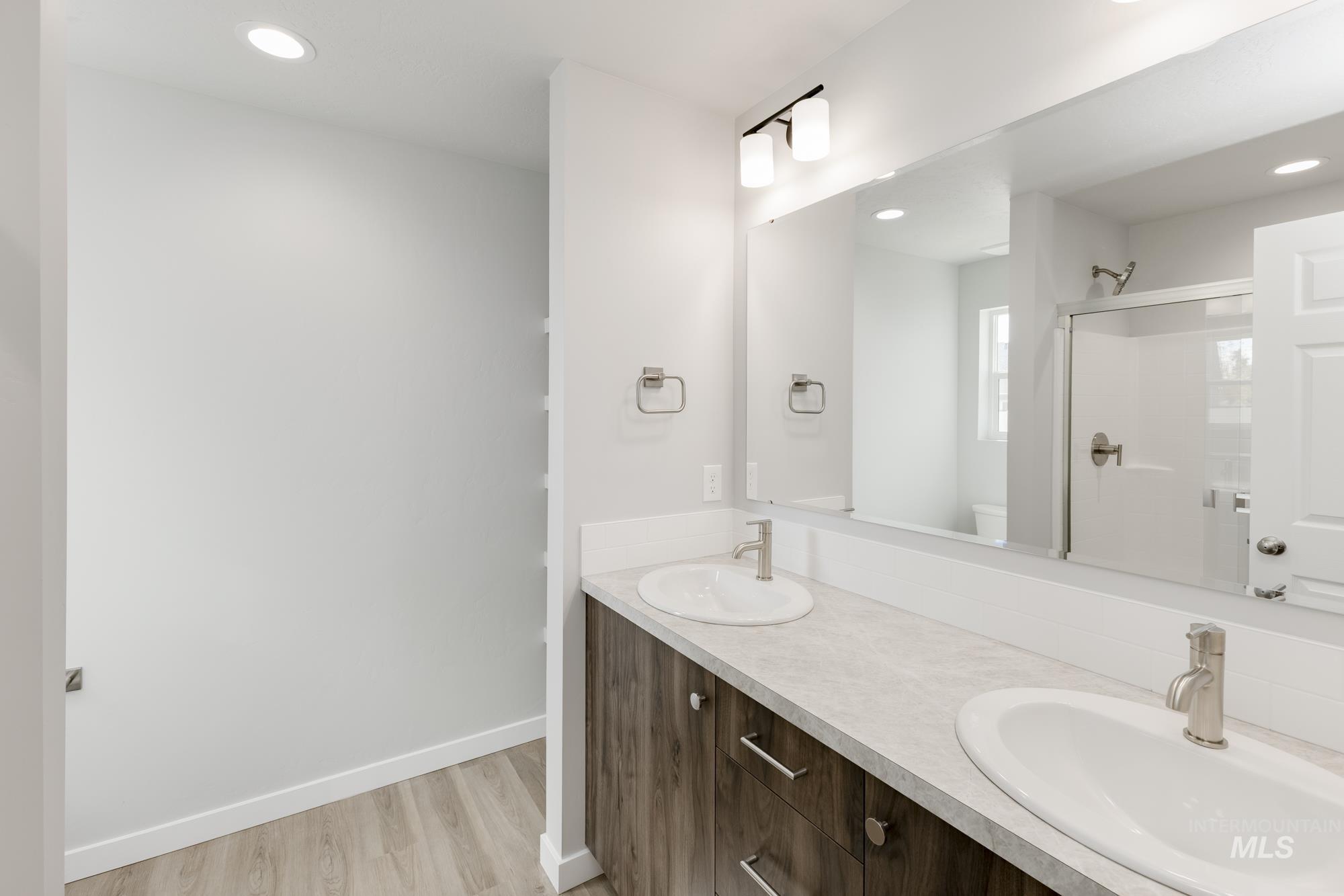 Bathroom with recessed lighting, double vanity, light wood-style flooring, and a shower stall