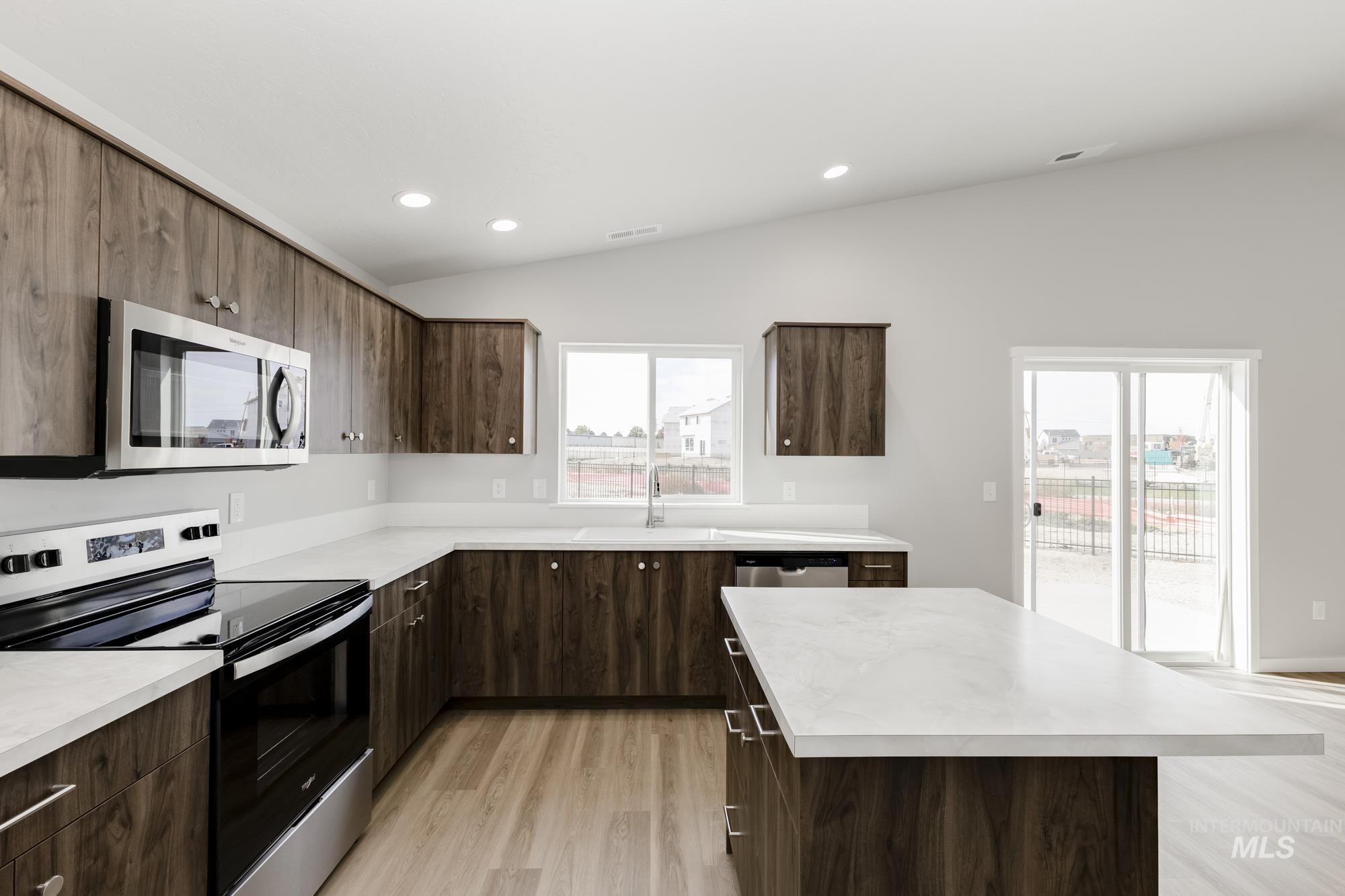 Kitchen with appliances with stainless steel finishes, lofted ceiling, light countertops, light wood finished floors, and dark brown cabinets