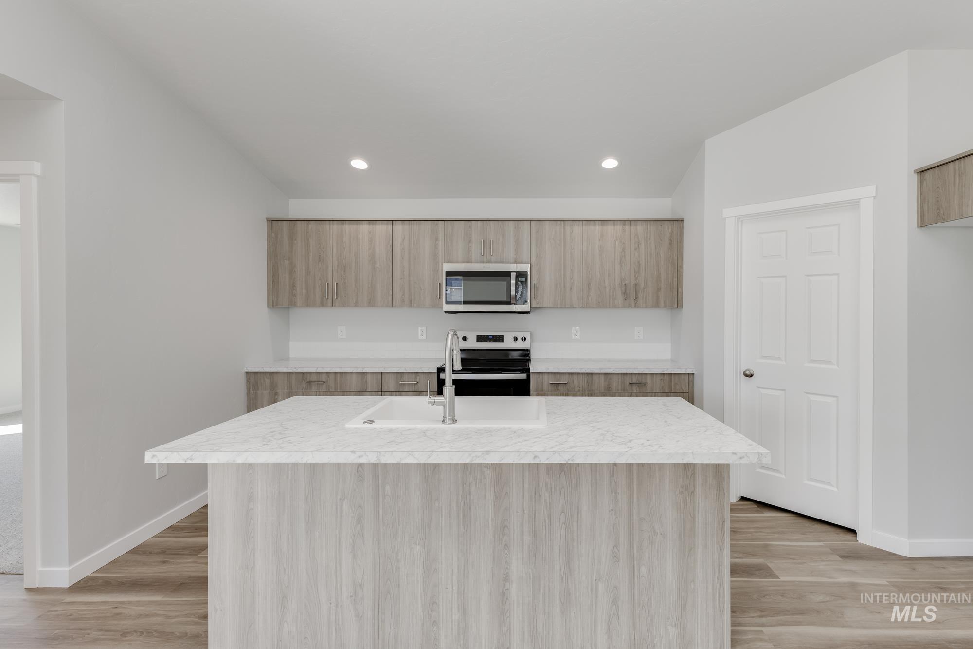 Kitchen with stainless steel appliances, an island with sink, modern cabinets, light wood-style flooring, and recessed lighting