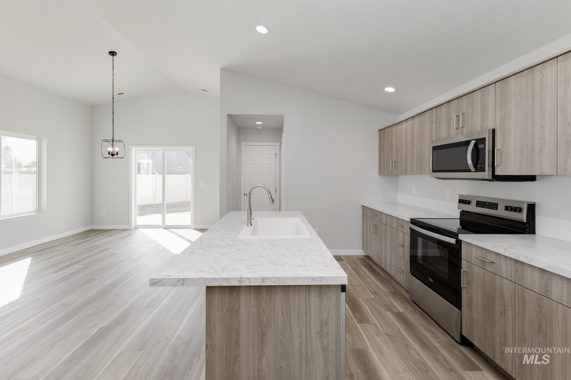 Kitchen with appliances with stainless steel finishes, light wood-type flooring, light brown cabinetry, lofted ceiling, and modern cabinets
