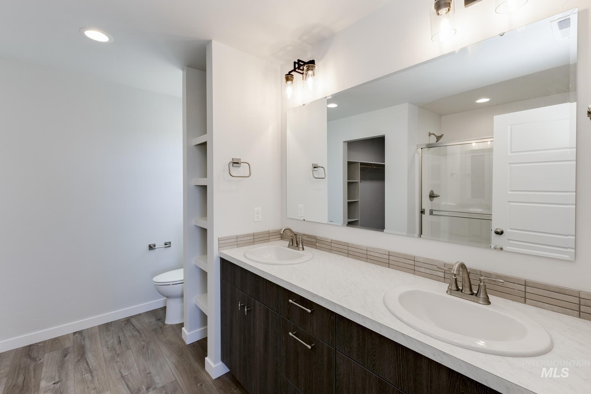 Bathroom featuring a shower stall, double vanity, a walk in closet, light wood-type flooring, and recessed lighting