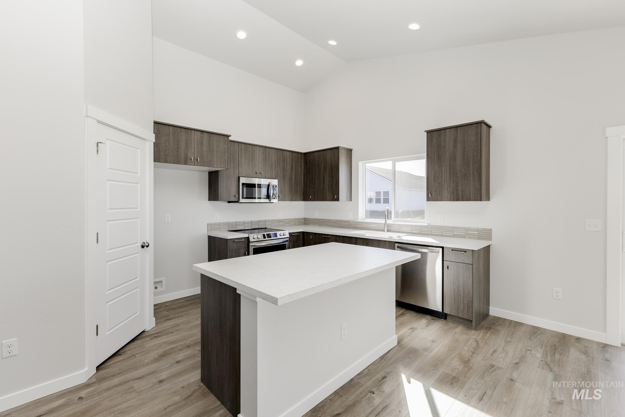 Kitchen featuring dark brown cabinetry, light countertops, a kitchen island, high vaulted ceiling, and appliances with stainless steel finishes