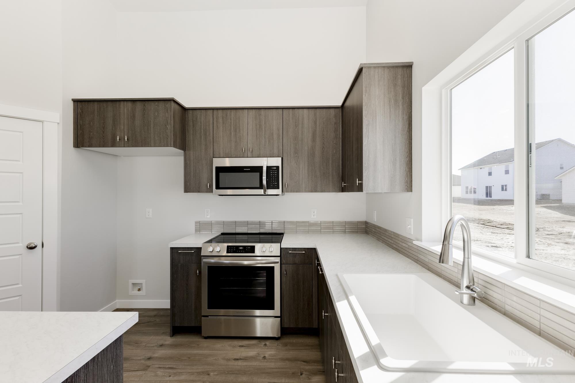Kitchen with dark brown cabinets, appliances with stainless steel finishes, light countertops, dark wood-type flooring, and a towering ceiling