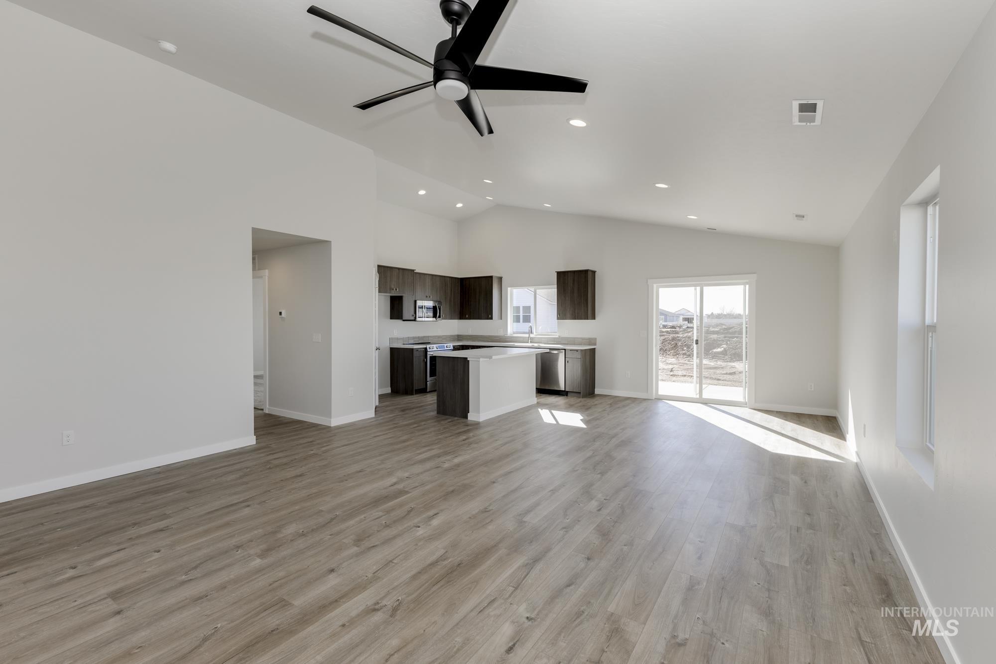 Unfurnished living room featuring light wood finished floors, a ceiling fan, high vaulted ceiling, and recessed lighting