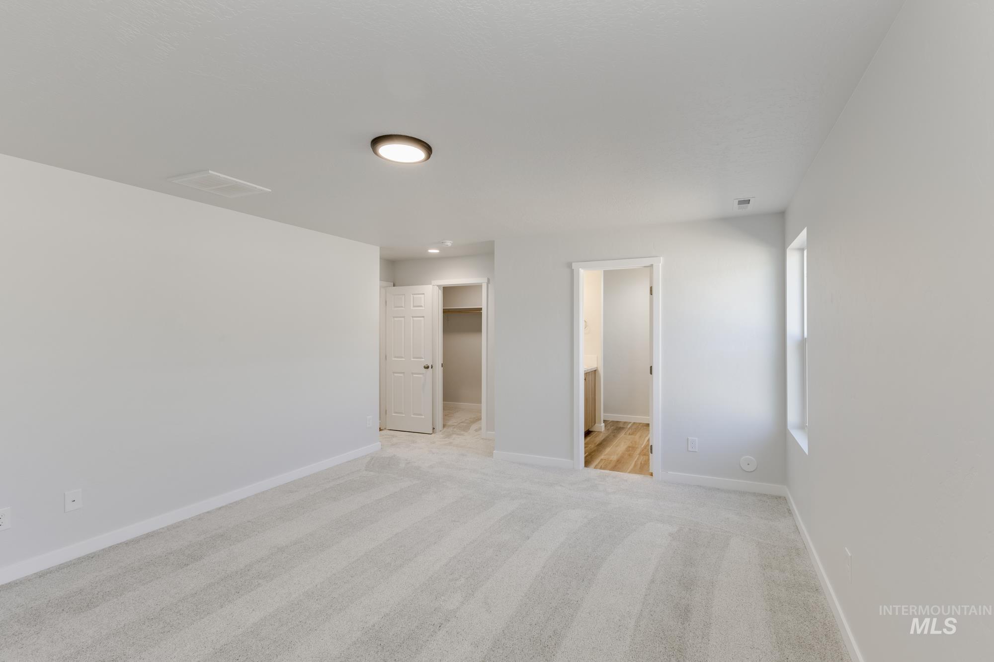 Unfurnished bedroom featuring a walk in closet, light colored carpet, and ensuite bathroom
