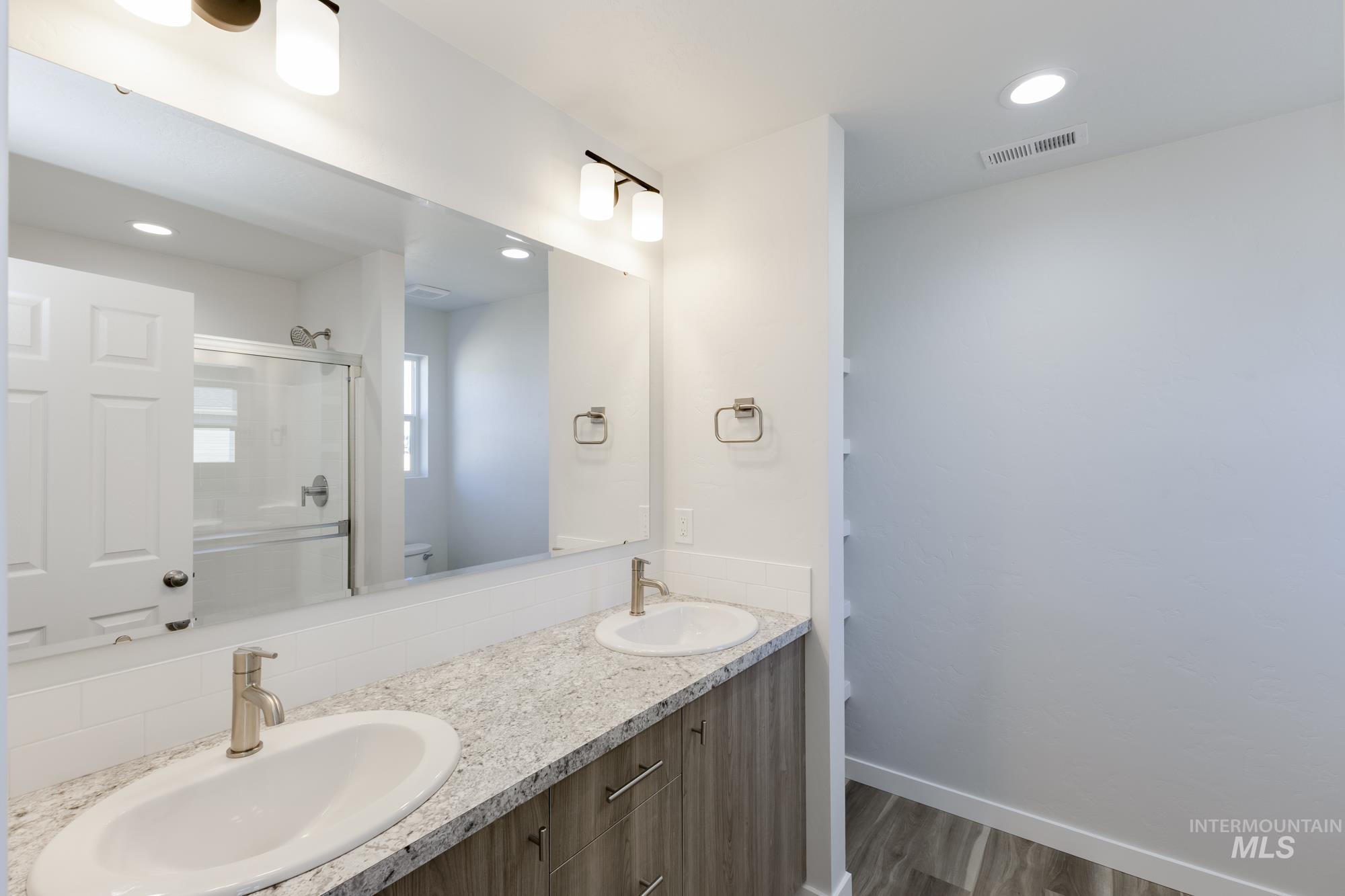 Bathroom featuring dark wood-style flooring, a stall shower, recessed lighting, and double vanity