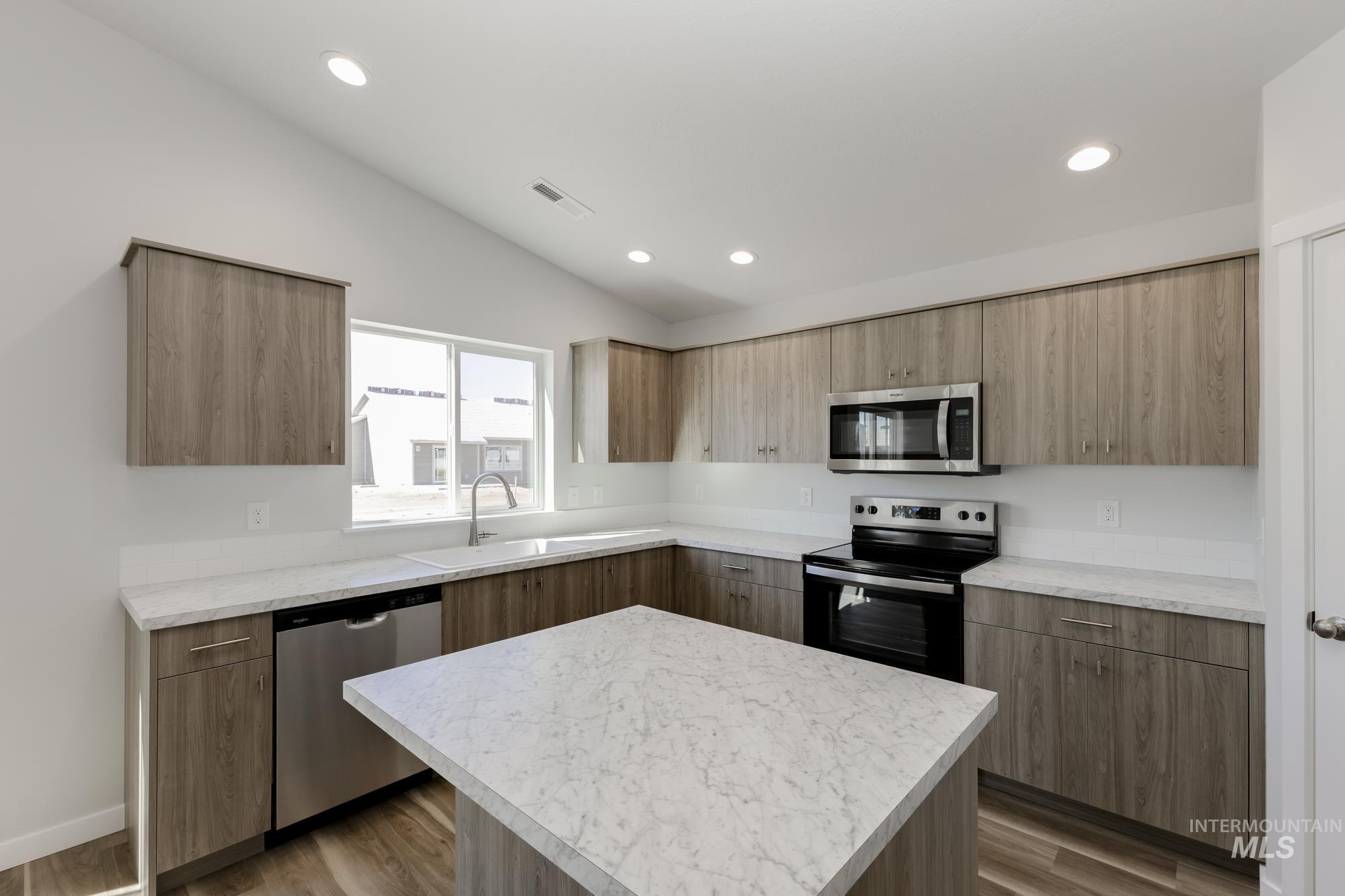 Kitchen featuring appliances with stainless steel finishes, light countertops, vaulted ceiling, light wood finished floors, and recessed lighting