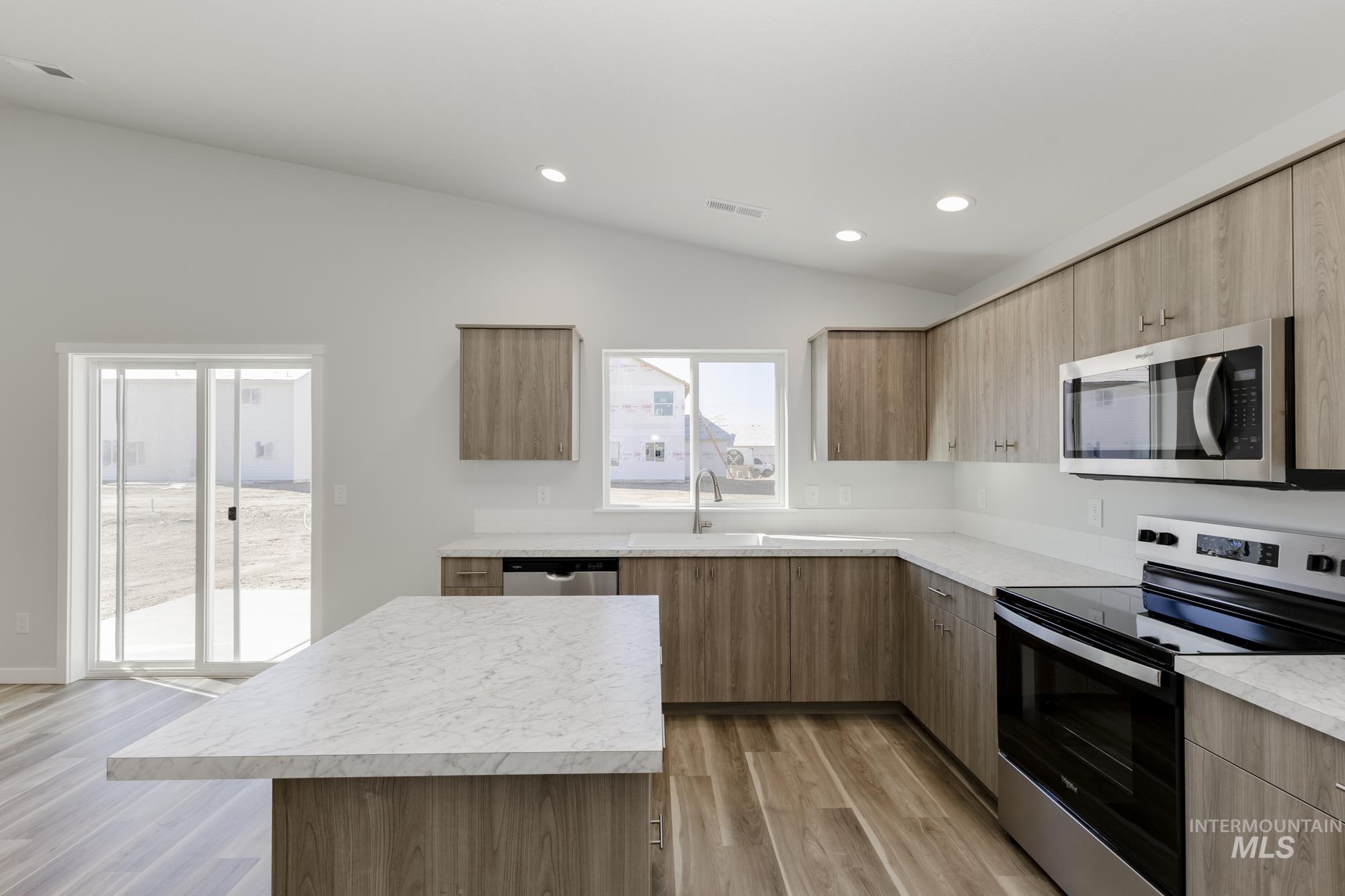 Kitchen with appliances with stainless steel finishes, lofted ceiling, light wood-type flooring, light countertops, and modern cabinets