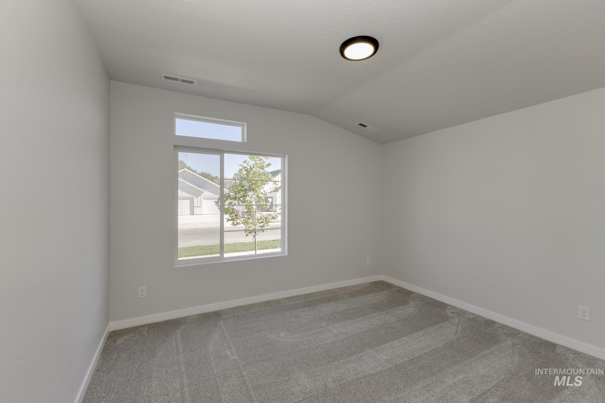 Unfurnished room featuring light carpet and lofted ceiling