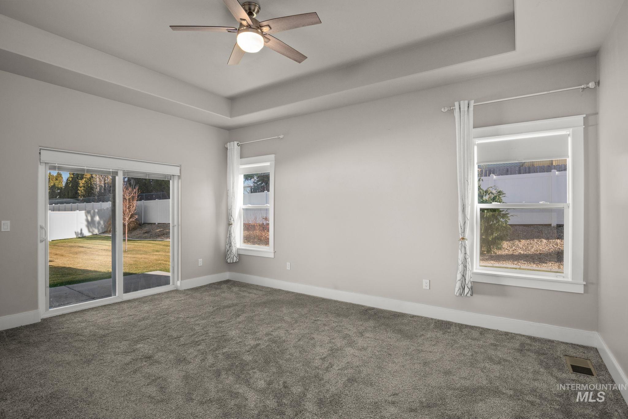 Carpeted empty room featuring a tray ceiling, a ceiling fan, and plenty of natural light