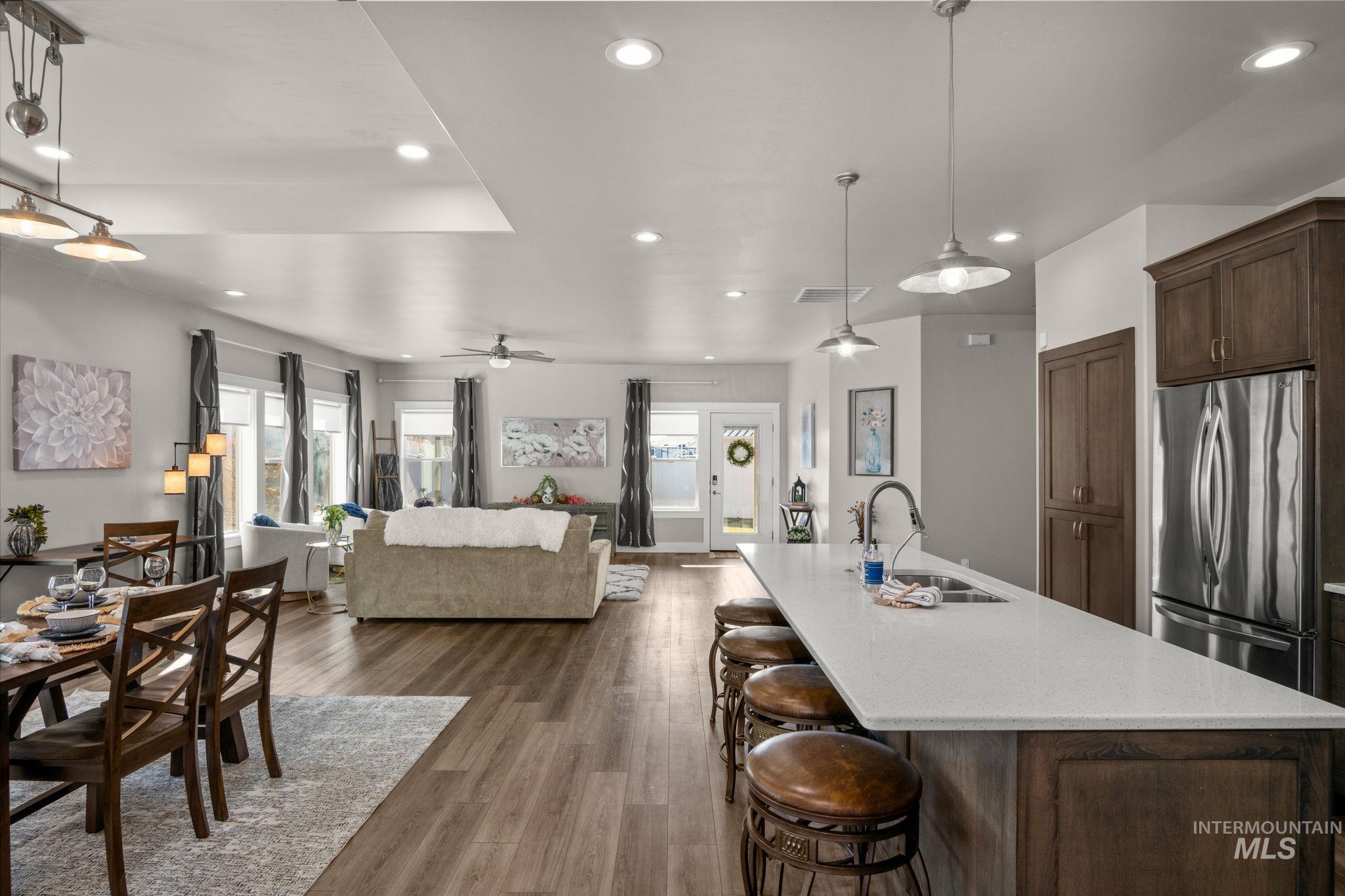 Kitchen with open floor plan, decorative light fixtures, freestanding refrigerator, a kitchen bar, and an island with sink