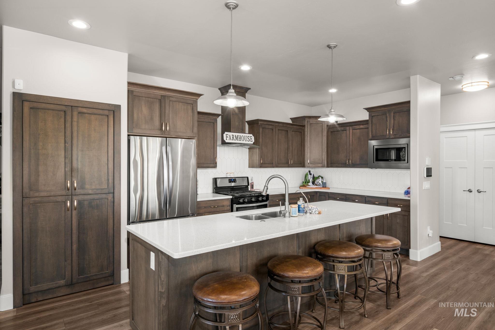 Kitchen featuring stainless steel appliances, decorative light fixtures, dark brown cabinetry, a kitchen bar, and an island with sink