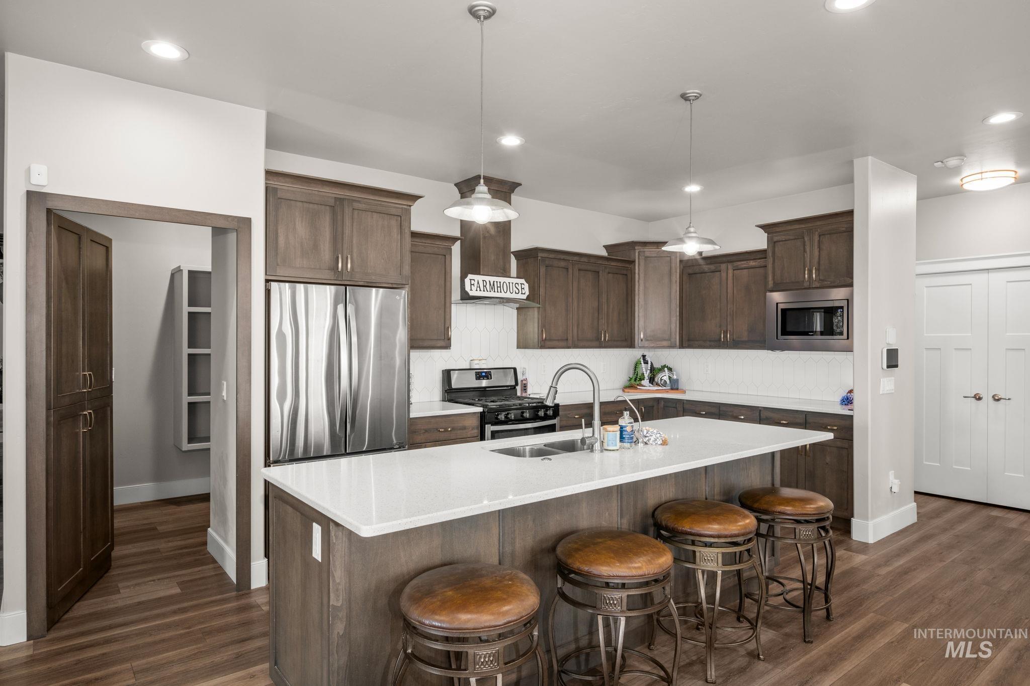 Kitchen featuring stainless steel appliances, decorative light fixtures, a kitchen breakfast bar, dark brown cabinetry, and a kitchen island with sink