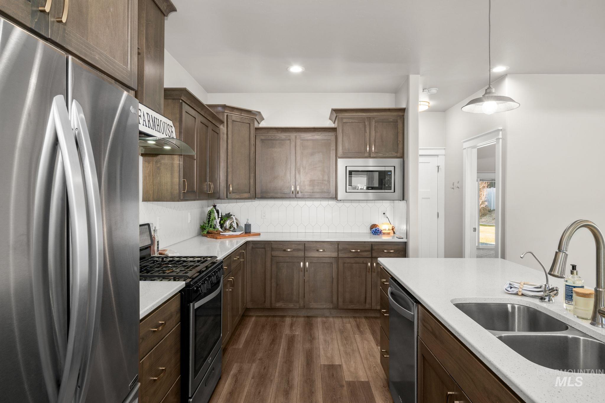 Kitchen featuring stainless steel appliances, dark brown cabinetry, hanging light fixtures, dark wood-style floors, and recessed lighting