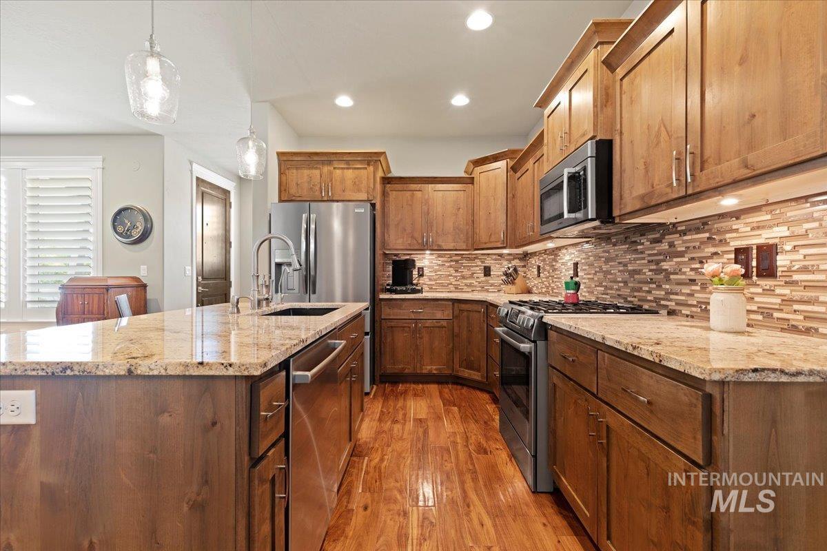 Kitchen with stainless steel appliances, wood finished floors, hanging light fixtures, decorative backsplash, and recessed lighting