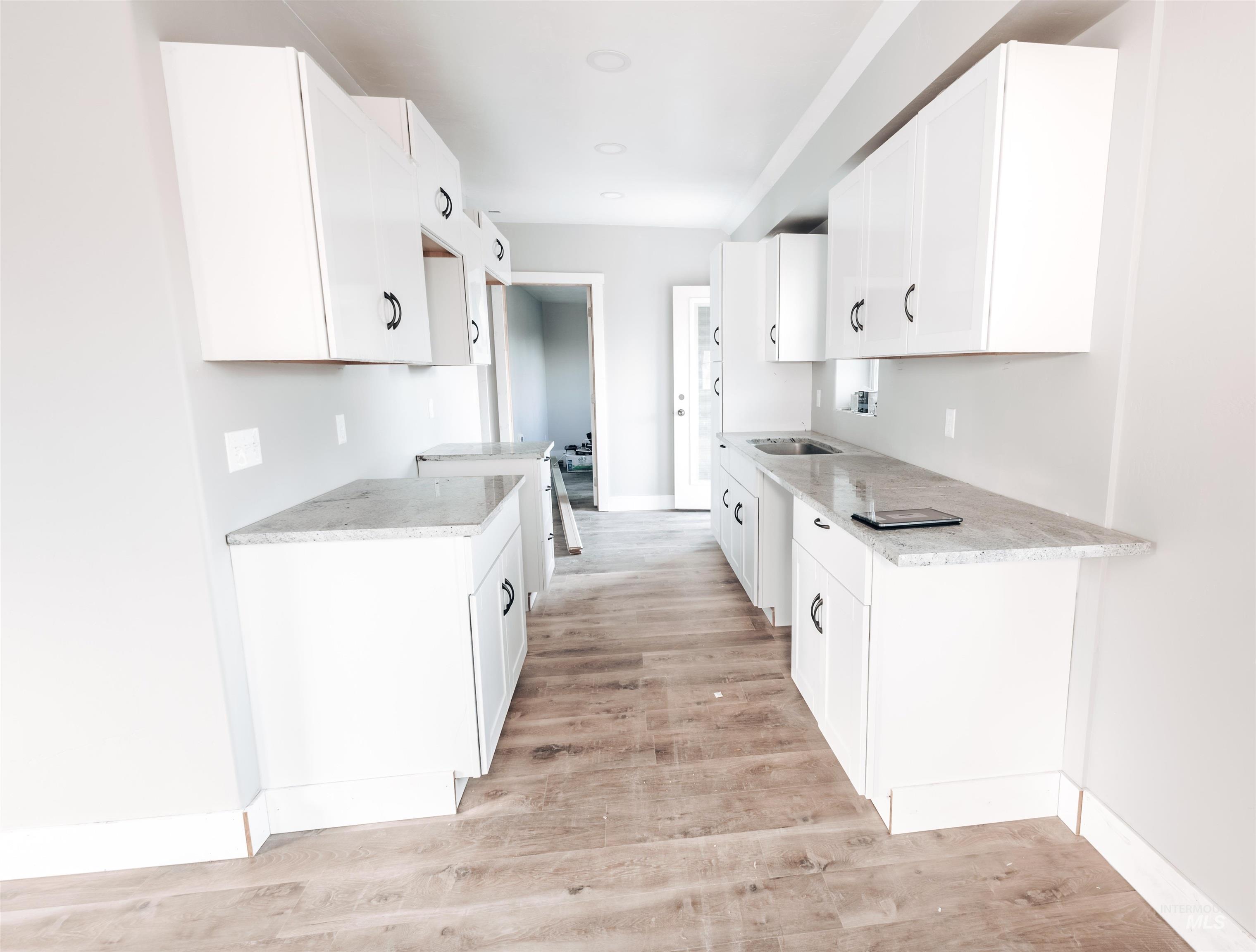 Kitchen with white cabinets, light stone countertops, and light wood-style flooring