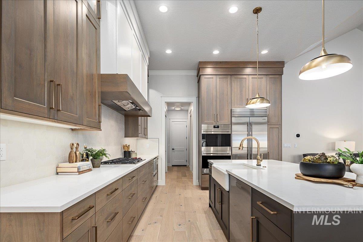 Kitchen featuring hanging light fixtures, an island with sink, light stone countertops, light wood-type flooring, and range hood