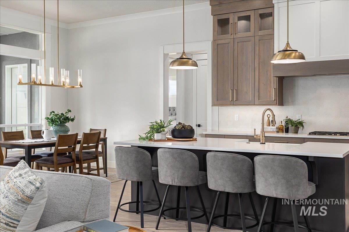 Kitchen with crown molding, decorative light fixtures, light stone countertops, a breakfast bar area, and a kitchen island with sink