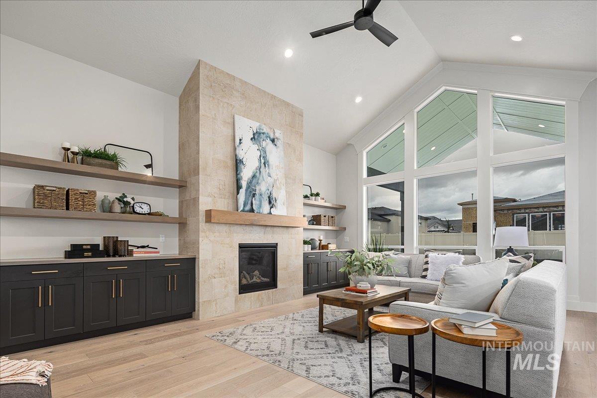 Living area featuring light wood finished floors, a fireplace, high vaulted ceiling, and a ceiling fan
