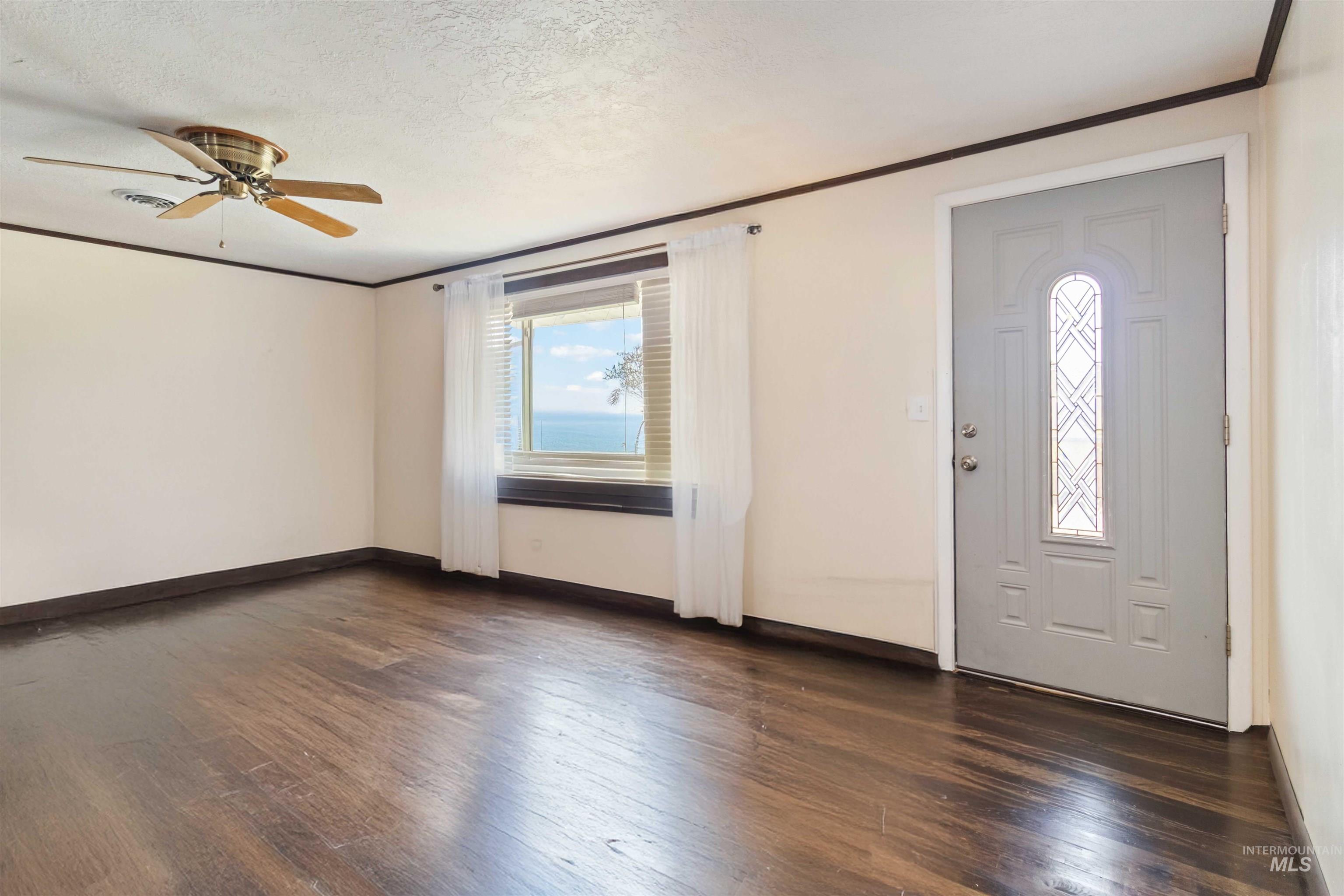 Foyer entrance featuring dark wood-type flooring, ornamental molding, a textured ceiling, and a ceiling fan