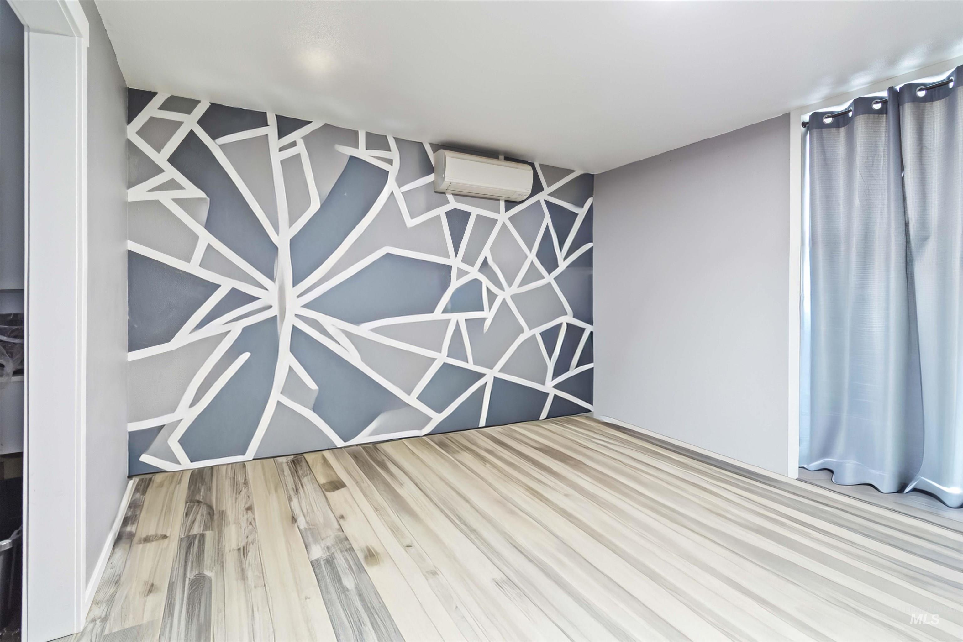 Empty room with an accent wall, light wood-type flooring, and an AC wall unit