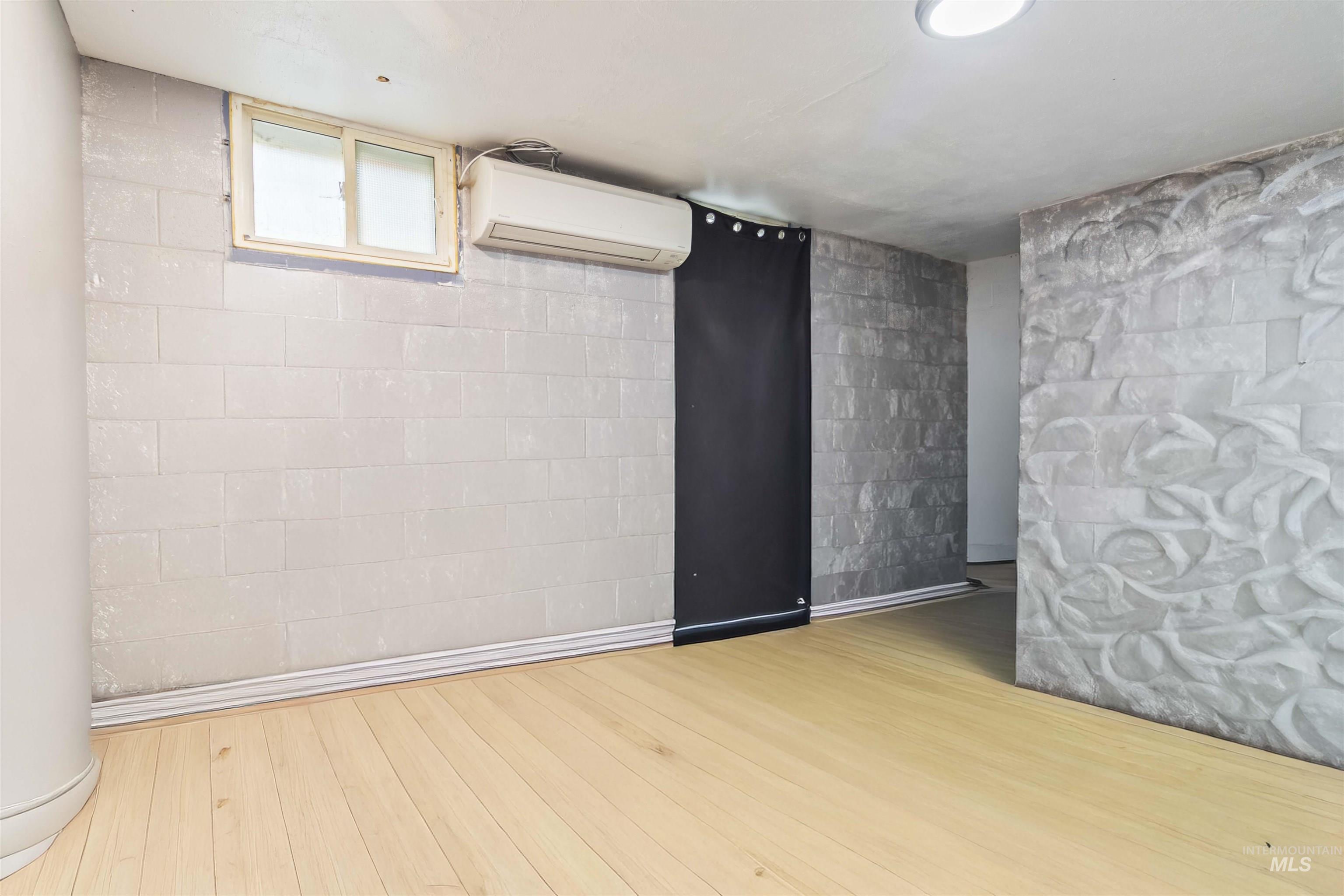 Unfurnished room featuring concrete block wall, a wall mounted AC, and wood finished floors