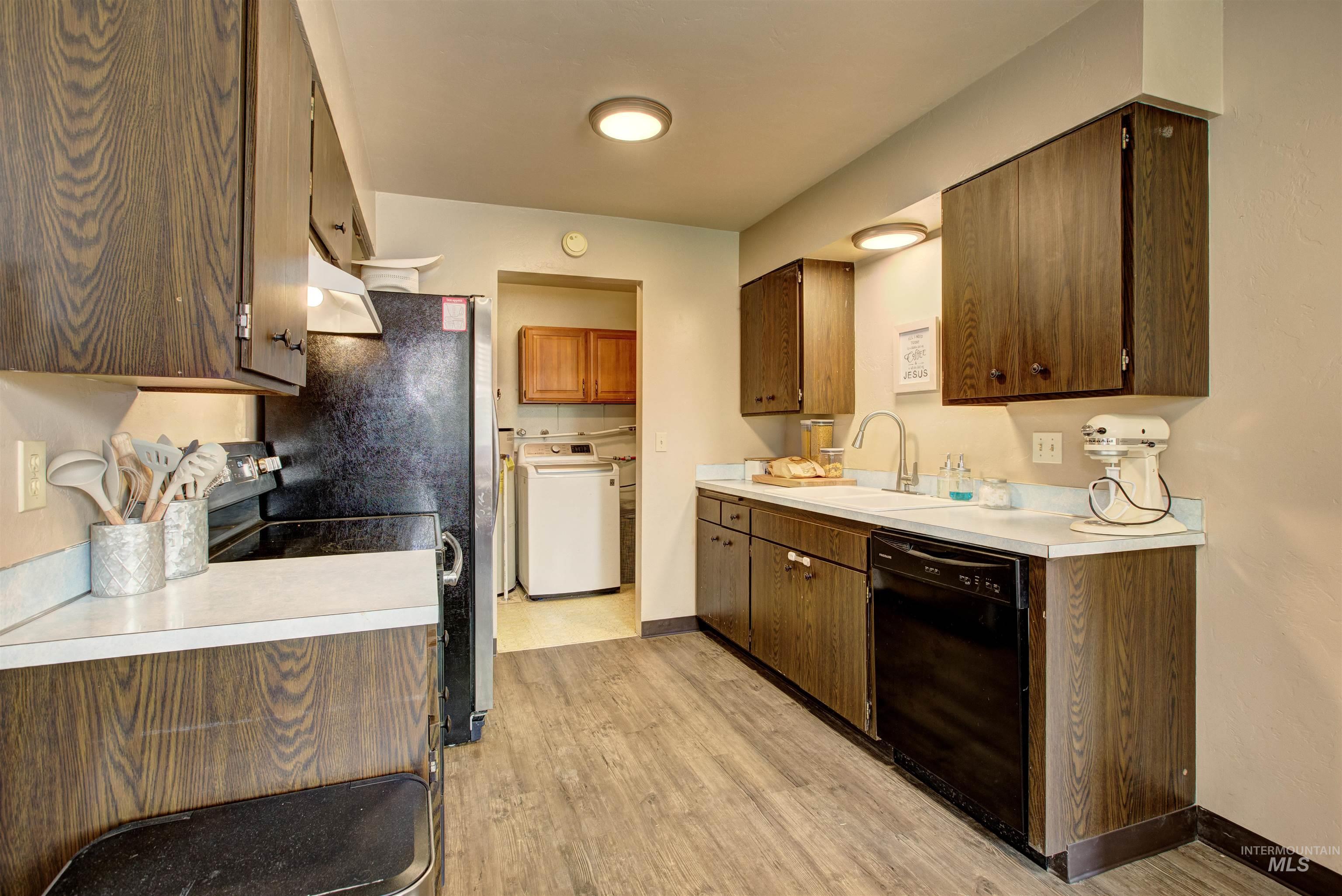 Kitchen with washer / clothes dryer, light countertops, black appliances, light wood-type flooring, and under cabinet range hood