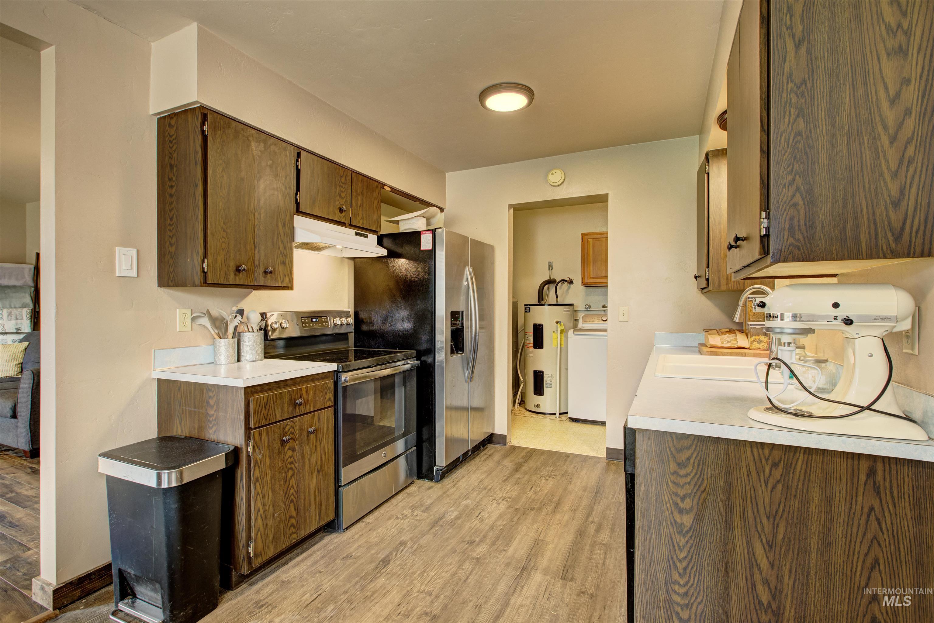 Kitchen with stainless steel range with electric cooktop, light countertops, electric water heater, light wood-style flooring, and under cabinet range hood