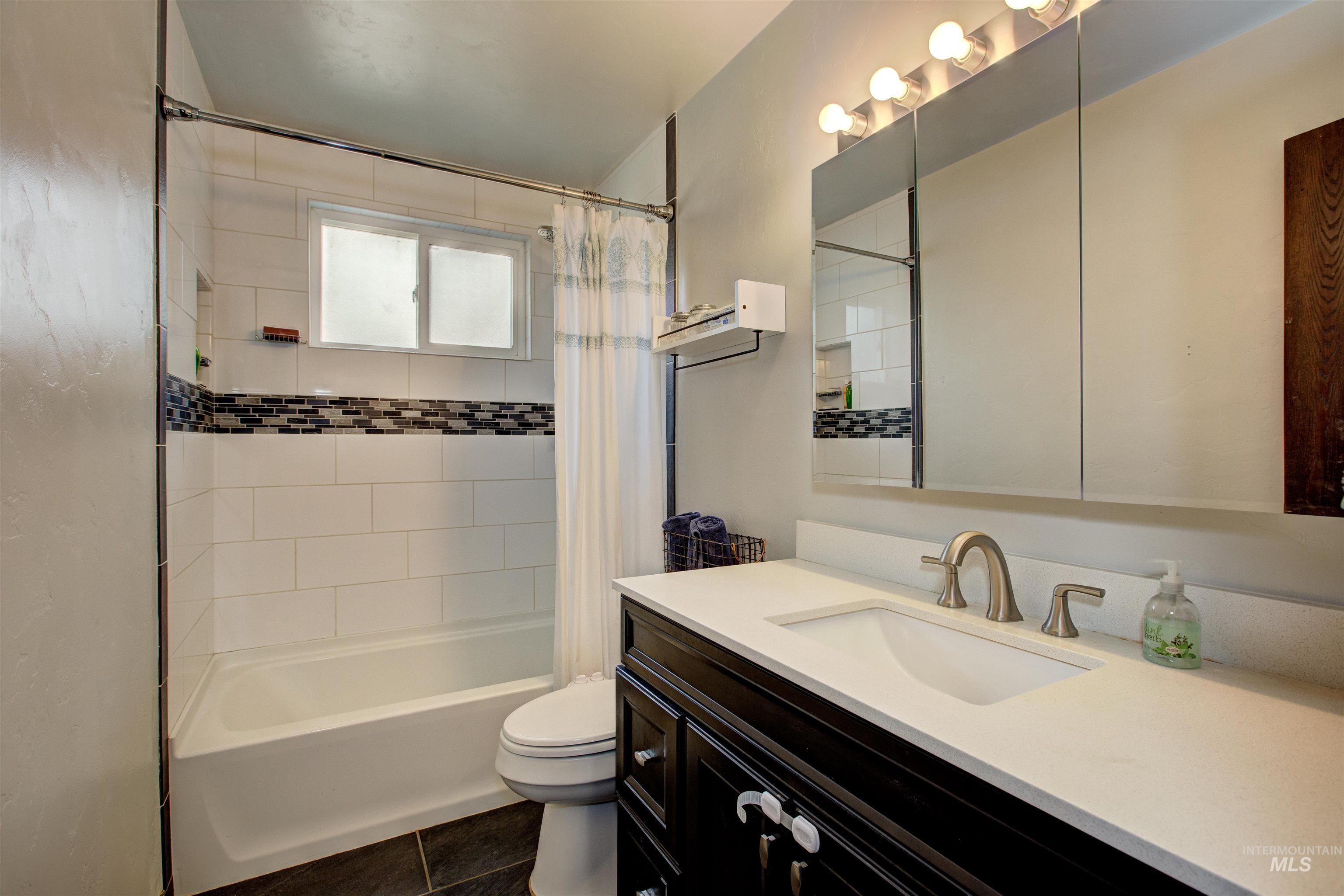 Bathroom with shower / tub combo with curtain, vanity, and dark tile patterned flooring