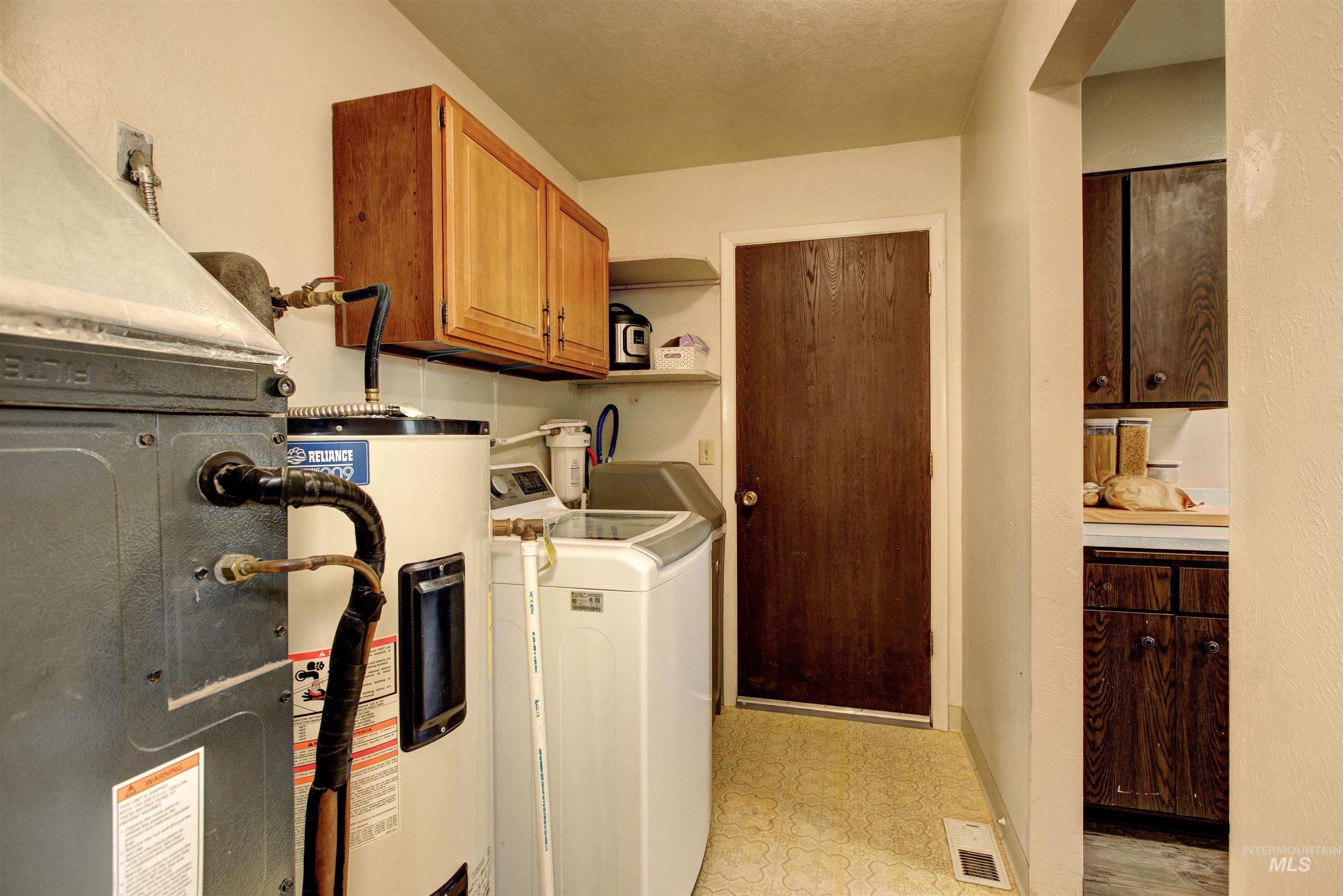 Laundry room with light flooring, washing machine and dryer, electric water heater, heating unit, and cabinet space