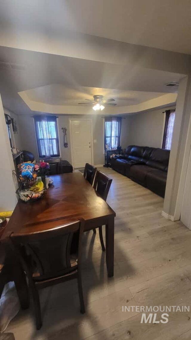 Dining area featuring a raised ceiling, light wood-style flooring, and a ceiling fan