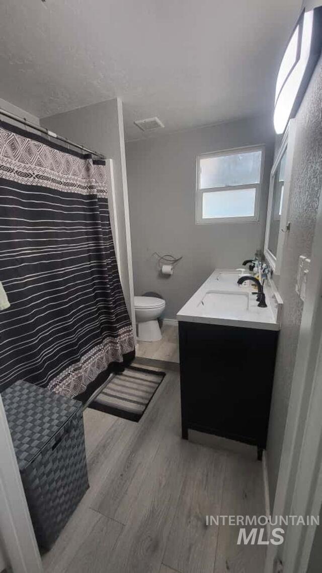 Full bath with a shower with curtain, double vanity, and light wood finished floors