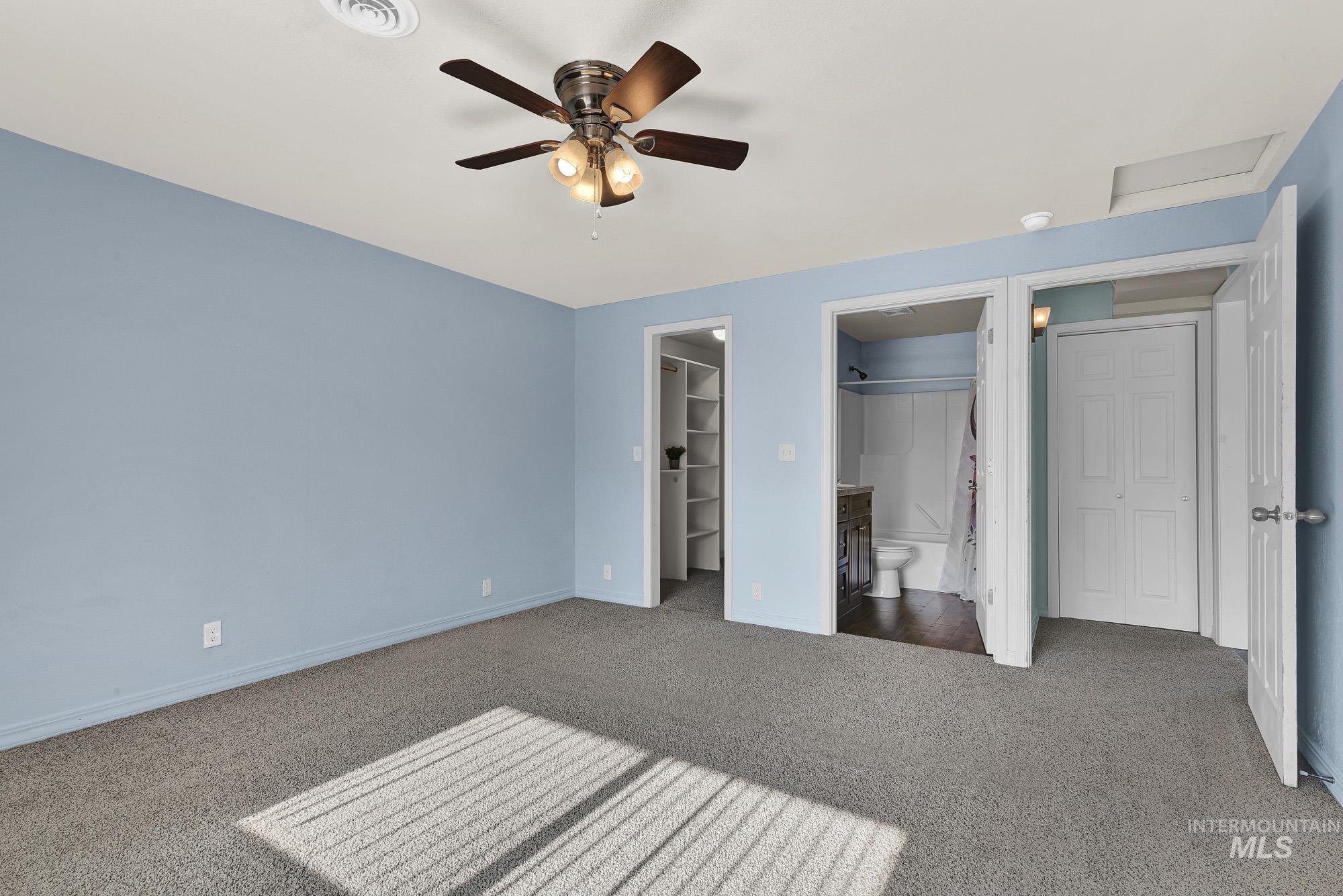 Primary bedroom suite with new carpet flooring, connected bathroom, ceiling fan, and a walk in closet