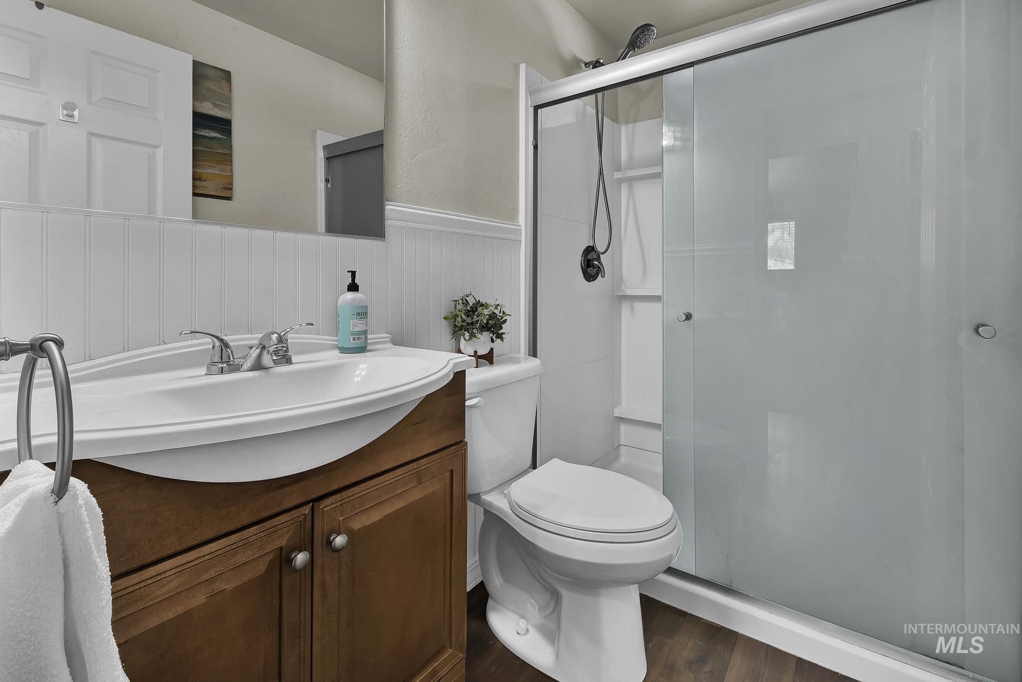 Bathroom featuring a wainscoted wall, vanity, a shower stall, and laminate wood like finished floors