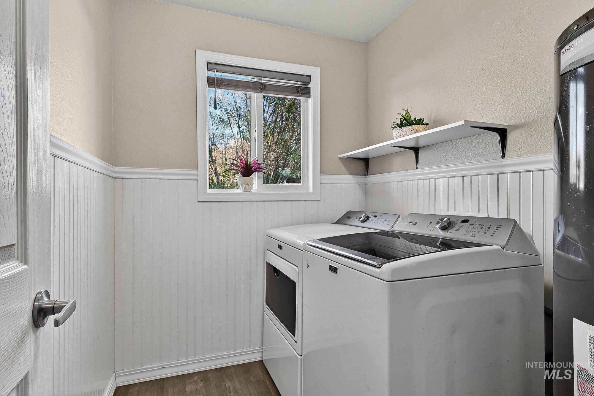 Laundry room featuring wainscoting, water heater, laminate wood-style flooring, and washer and clothes dryer area