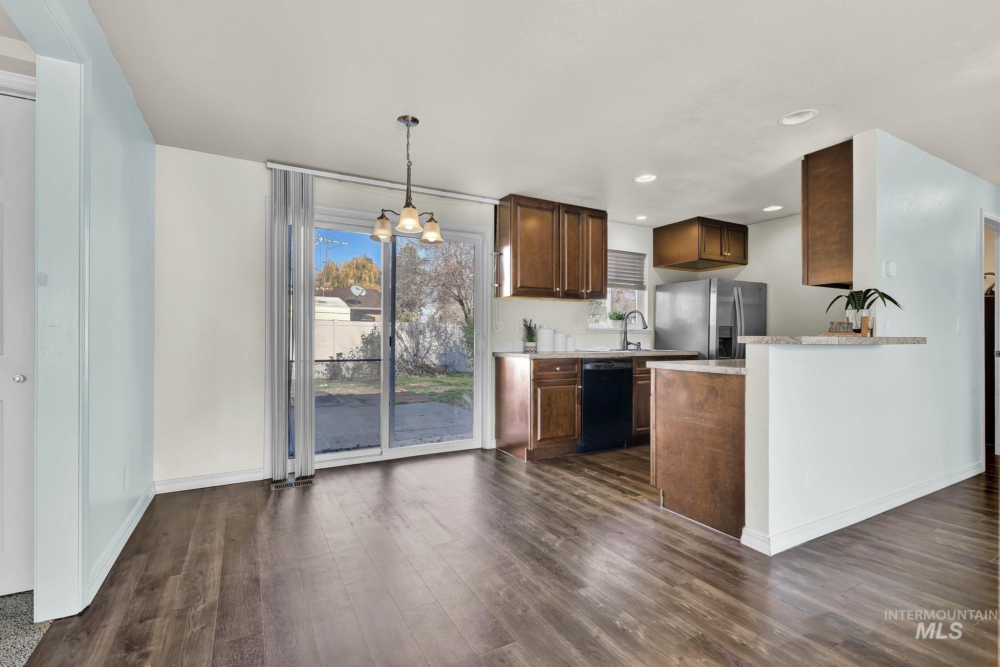 Kitchen featuring a chandelier, light laminate counters, stainless steel refrigerator with ice dispenser,  laminate wood-style floors, and black dishwasher