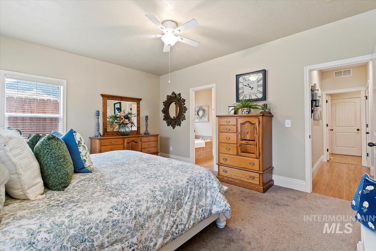 Bedroom with light colored carpet, ceiling fan, and ensuite bathroom