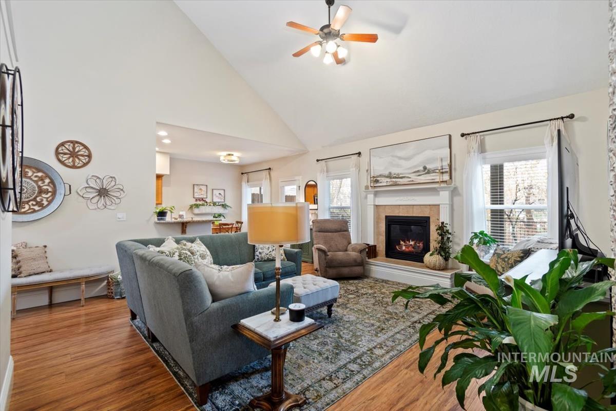 Living room with high vaulted ceiling, wood finished floors, a fireplace, and a ceiling fan