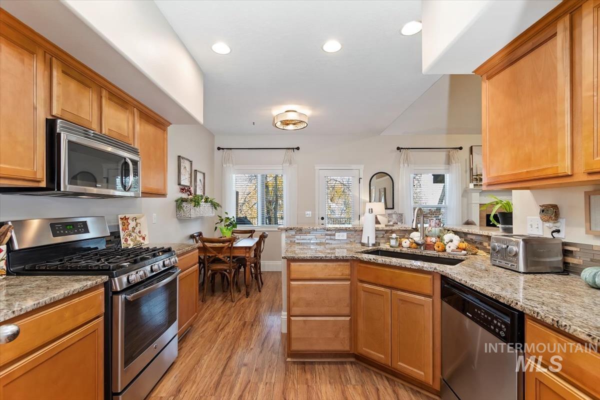 Kitchen with appliances with stainless steel finishes, a peninsula, light stone counters, healthy amount of natural light, and recessed lighting