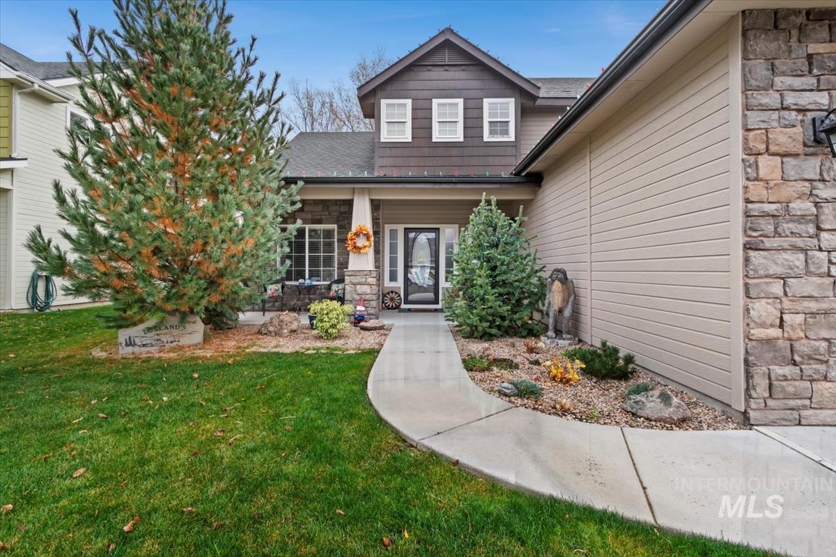 View of exterior entry featuring stone siding, a yard, covered porch, and roof with shingles