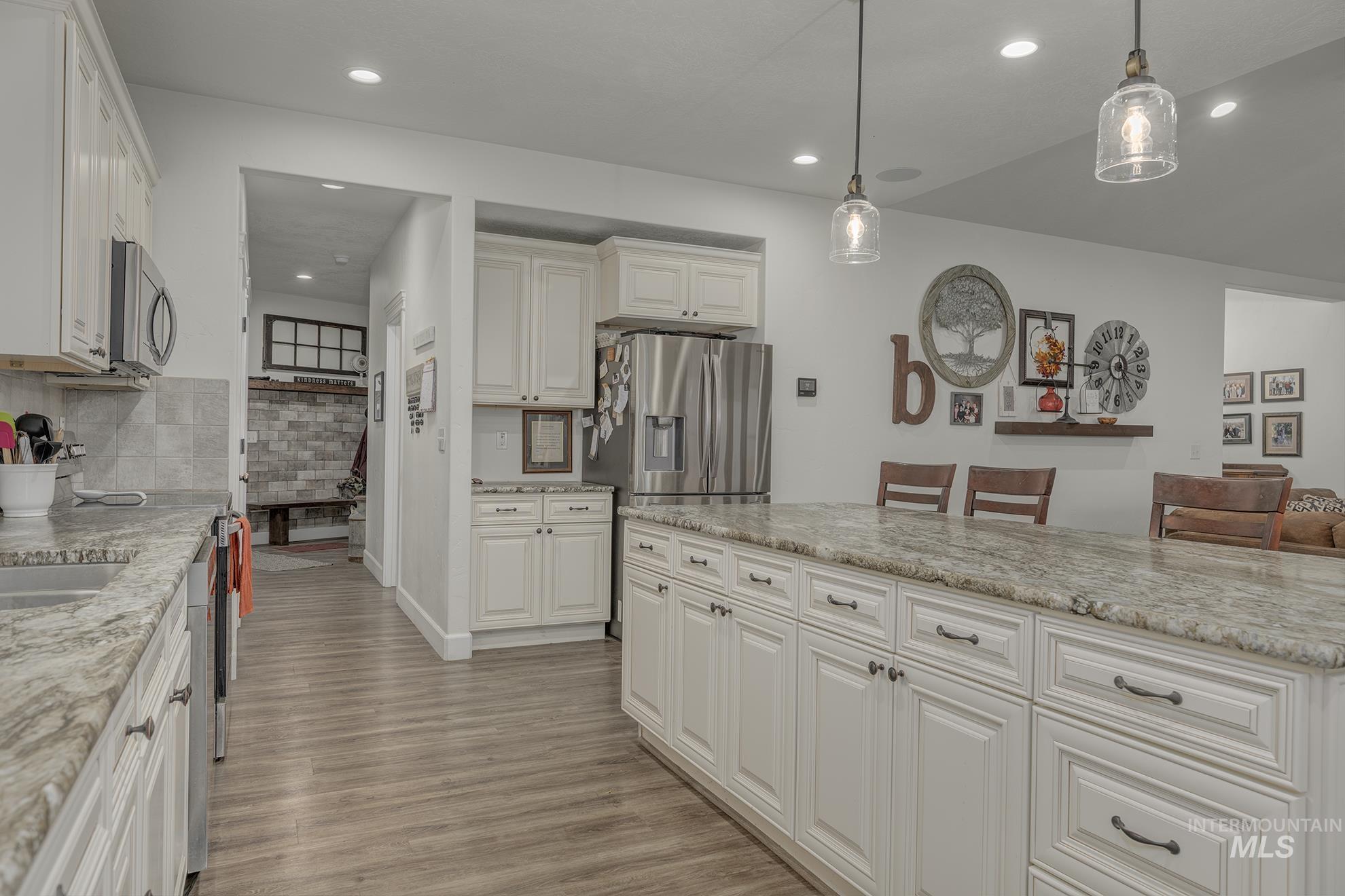 Kitchen with pendant lighting, recessed lighting, light wood-type flooring, a breakfast bar area, and light stone countertops