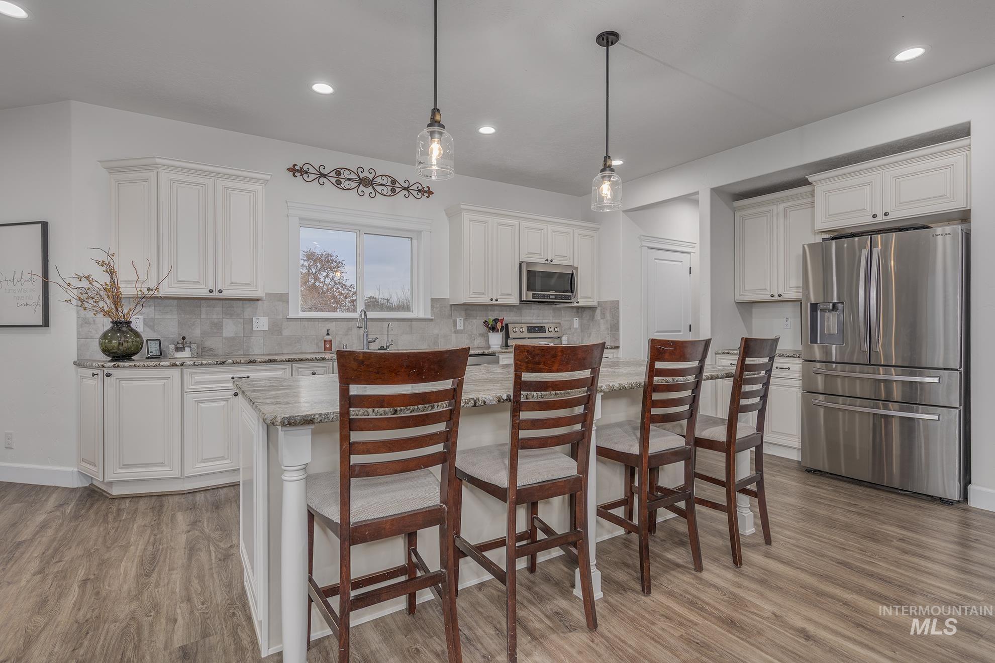 Kitchen with stainless steel appliances, pendant lighting, white cabinets, light stone countertops, and a kitchen breakfast bar