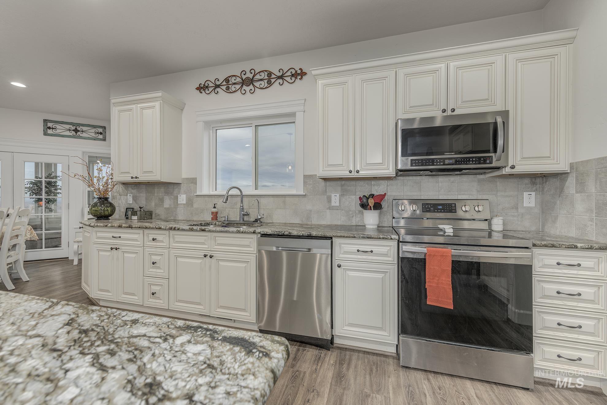 Kitchen with appliances with stainless steel finishes, light wood-type flooring, light stone countertops, backsplash, and plenty of natural light