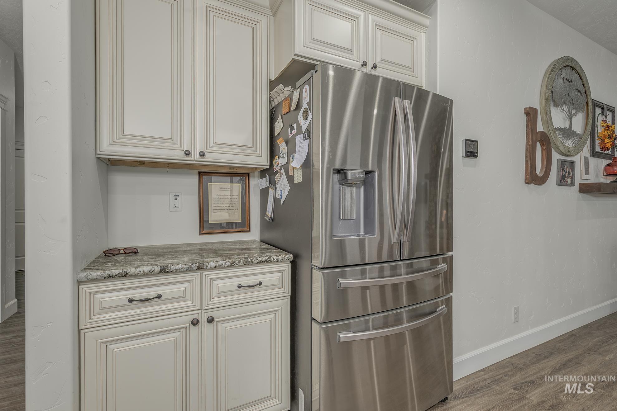 Kitchen with stainless steel fridge with ice dispenser, light wood-type flooring, light stone counters, and white cabinets
