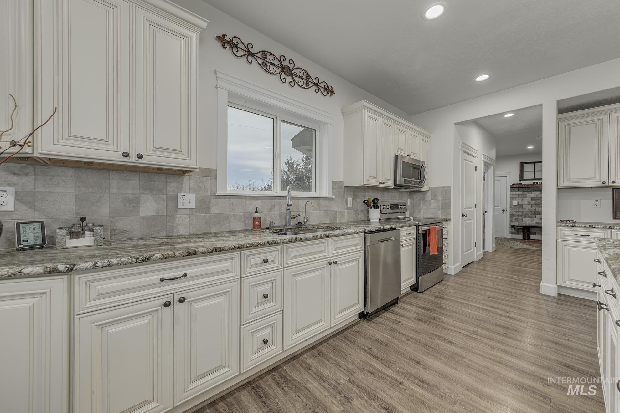 Kitchen with white cabinetry, appliances with stainless steel finishes, light wood-style flooring, backsplash, and recessed lighting